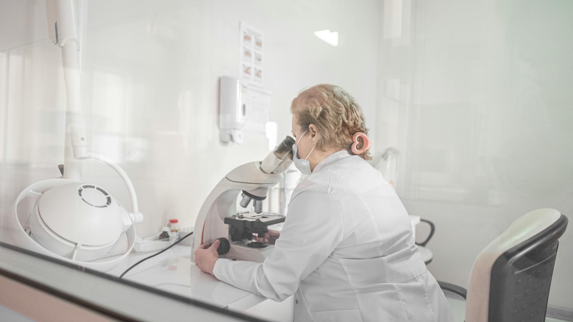 A scientist works with a microscope in a bright, modern lab setting, wearing a lab coat.