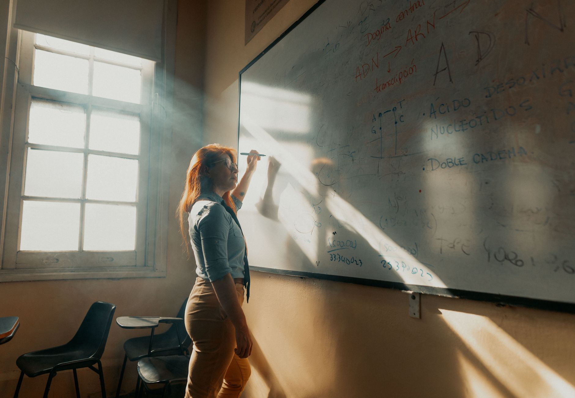 A teacher in Buenos Aires writes on a whiteboard in natural light streaming through a window.