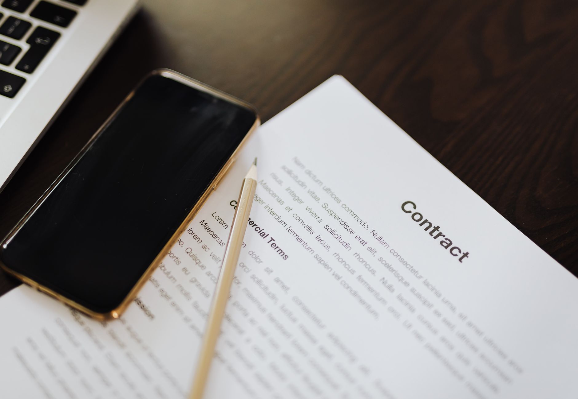 Close-up of a contract document alongside a smartphone and laptop, ideal for business concepts.